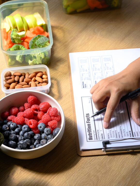 Nutritionist analyzing and writing a healthy meal plan with fresh fruits, vegetables, and nuts on the table.