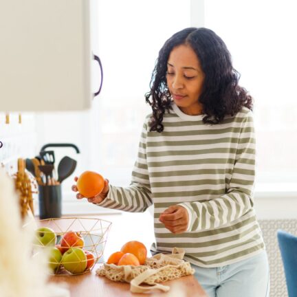 Woman holding orange near fruit bowl in kitchen