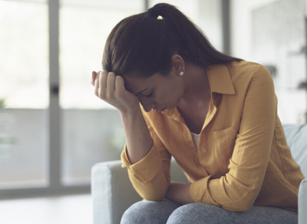 Depressed young woman sitting in the living room at home, she is feeling hopeless and sad