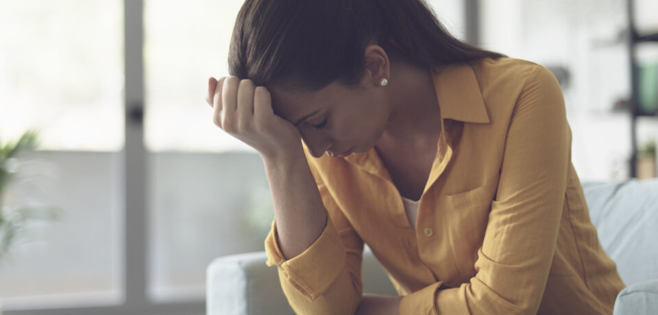 Depressed young woman sitting in the living room at home, she is feeling hopeless and sad