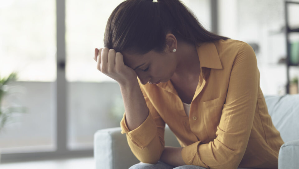 Depressed young woman sitting in the living room at home, she is feeling hopeless and sad