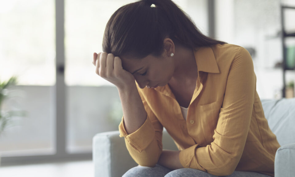 Depressed young woman sitting in the living room at home, she is feeling hopeless and sad